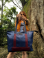 Wearsos Do Good Tote in blue and maroon upcycled aviation leather held by a woman in a forest setting